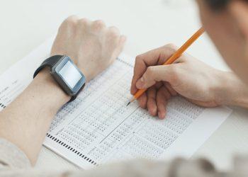 a person writing on white paper using pencil