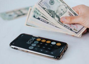 crop faceless person with cash and calculator app on smartphone