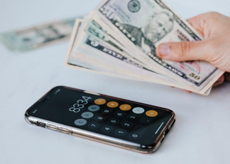 crop faceless person with cash and calculator app on smartphone